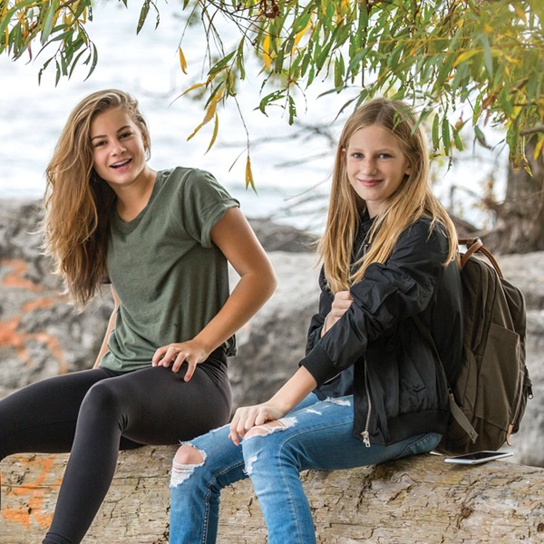 Two adolescent girls siting on rocks along the river.
